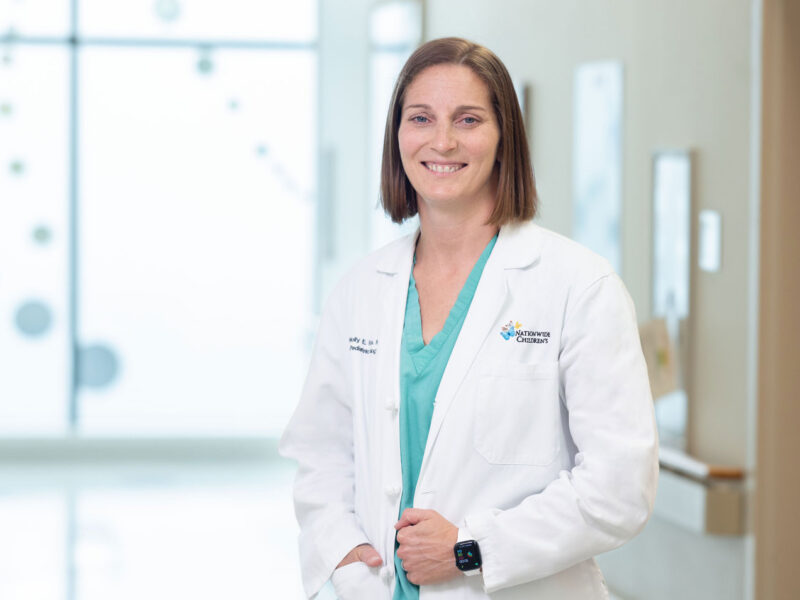Molly Fuchs, MD, chief of Urology at Nationwide Children's, wearing scrubs and a white coat standing in a hospital hallway.