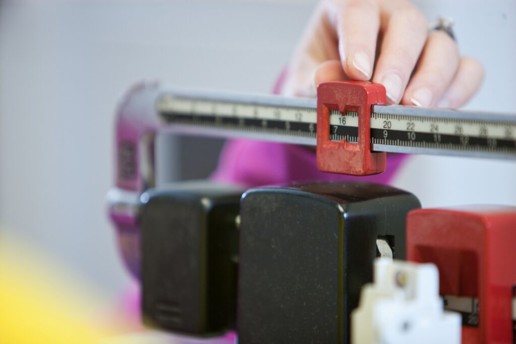 A hand adjusts the weight measurement on a doctor's scale in a healthcare setting.