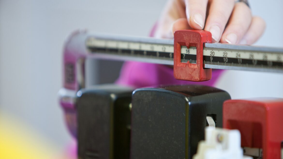 A hand adjusts the weight measurement on a doctor's scale in a healthcare setting.