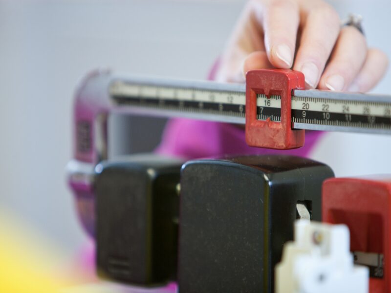 A hand adjusts the weight measurement on a doctor's scale in a healthcare setting.
