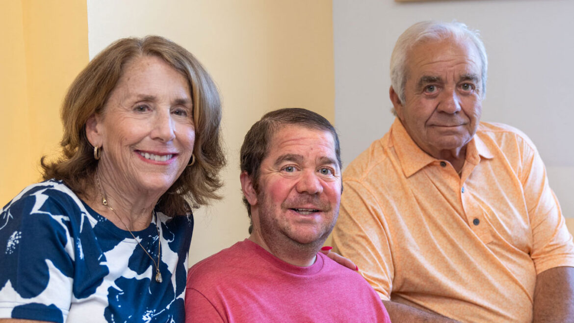 A man with Duchenne muscular dystrophy sits in a wheelchair between two family members