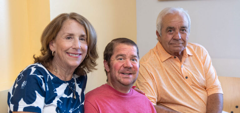 A man with Duchenne muscular dystrophy sits in a wheelchair between two family members