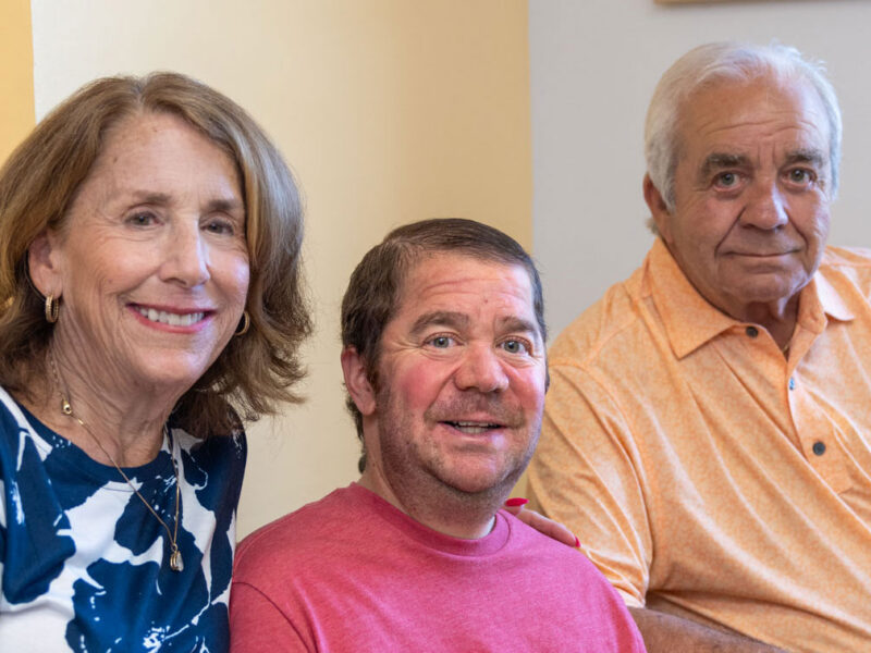 A man with Duchenne muscular dystrophy sits in a wheelchair between two family members