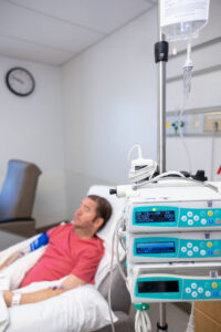 Infusion pumps and an IV bag stand in the foreground as a man with Duchenne muscular dystrophy receives treatment in the background.