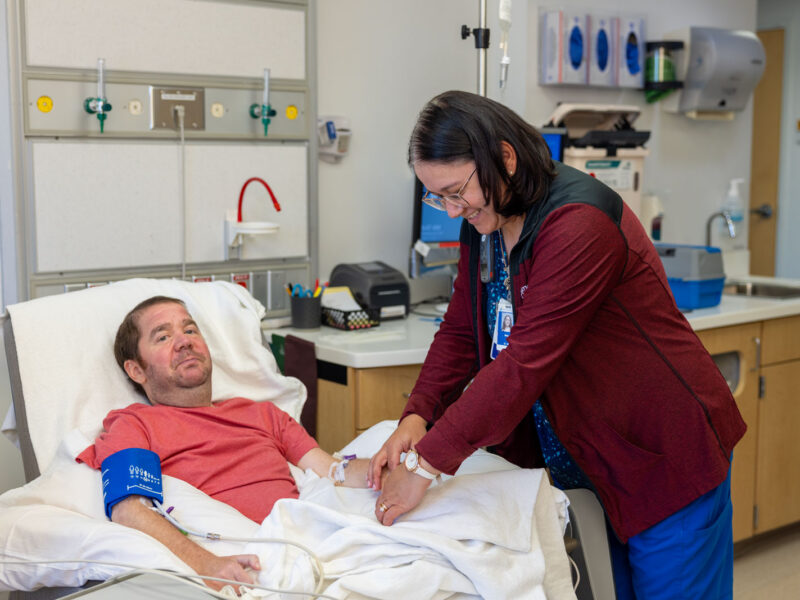 A nurse adjusts an intravenous line for a man with Duchenne muscular dystrophy reclining in a hospital infusion treatment room.