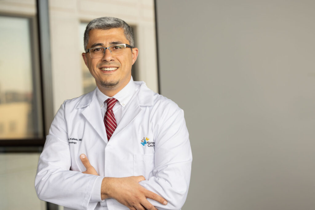 Dr. Kallash standing in an office hallway, wearing a white coat and red tie.