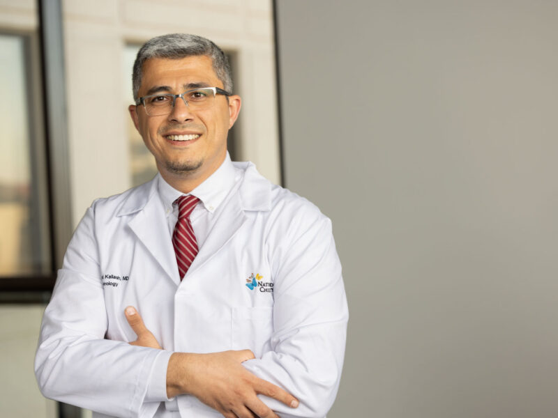 Dr. Kallash standing in an office hallway, wearing a white coat and red tie.
