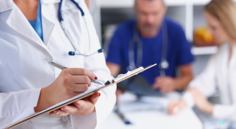 Doctor in a white coat holding a clipboard pad and fill medical history list with silver pen.