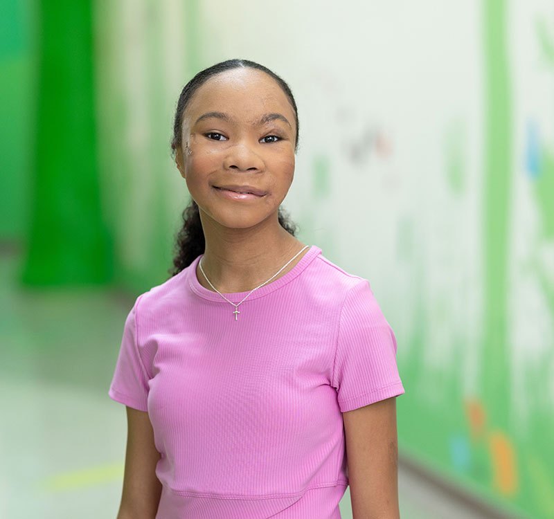 Smiling girl in pink shirt in a hospital hallway
