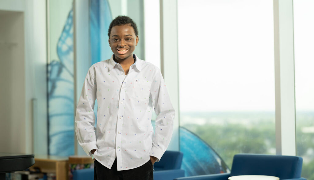 King Robinson - a young patient at Nationwide Children's - smiling and standing next to a window inside the hospital