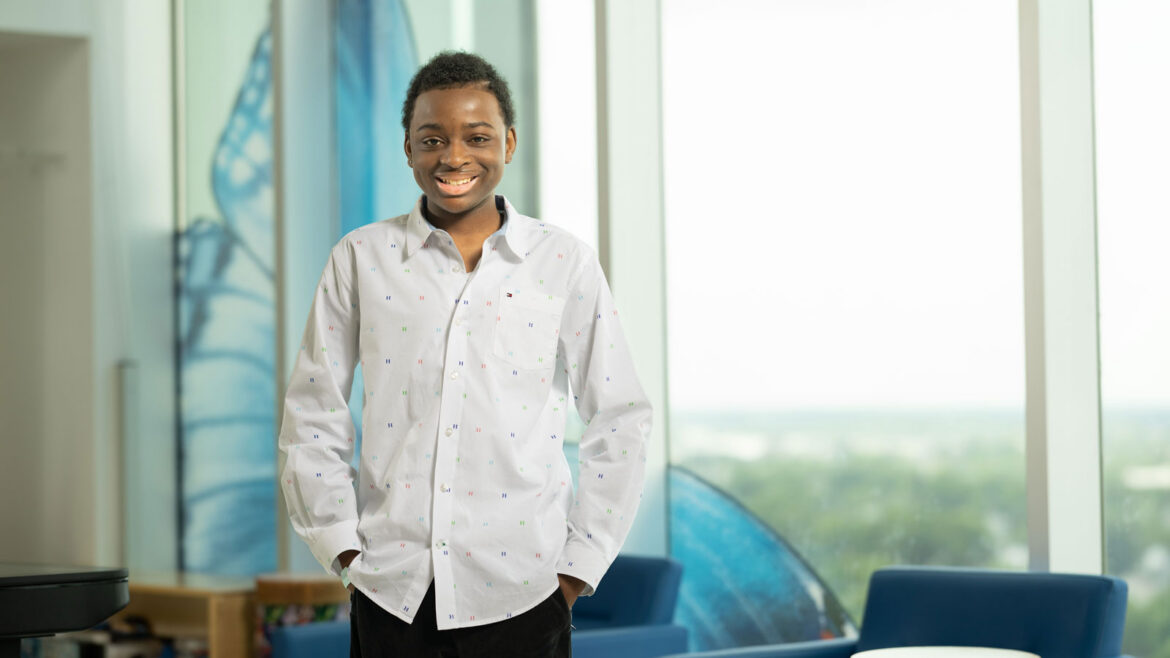 King Robinson - a young patient at Nationwide Children's - smiling and standing next to a window inside the hospital